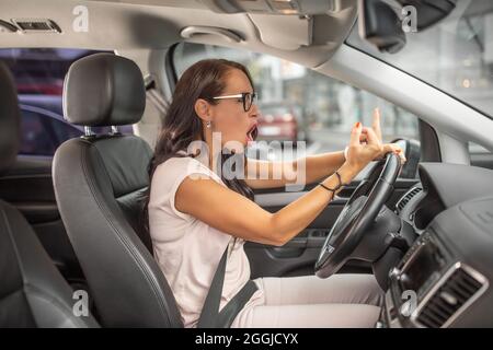 Weibliche verärgerte Fahrerin, die beim Fahren auf einem Parkplatz den Mittelfinger zeigt. Stockfoto