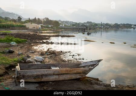 Traditionelles Holzkanu an der Küste entlang des Atitlan Sees bei Sonnenuntergang mit Blick auf nebelige vulkanische Berge in San Pedro la Laguna, Guatemala Stockfoto