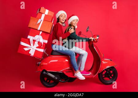 Foto von süßen lustigen Schulkinder gestrickt Pullover Reiten Moped tragen präsentiert isoliert roten Hintergrund gekleidet Stockfoto