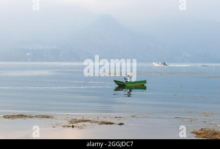 Santa Pedro la Laguna, Guatemala - 23. April 2018: Fischer im traditionellen hölzernen Kanu und Motorboot im Atitlan See bei Sonnenuntergang mit Blick auf neblig Stockfoto