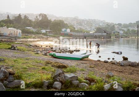 Santa Pedro la Laguna, Guatemala - 23. April 2018: Einheimische Jungen, die bei Sonnenuntergang an der Küste entlang des Atitlan-Sees fischen, mit Blick auf neblige vulkanische Berge Stockfoto