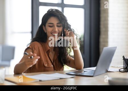 Junge Geschäftsfrau, die vom Heimbüro aus am Mobiltelefon spricht und an einem Laptop arbeitet, diskutiert über Arbeitsfragen aus der Ferne Stockfoto