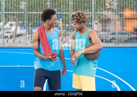 Freunde afroamerikanischer Basketballspieler, die das Training auf dem Platz beenden, reden und lachen. Stockfoto