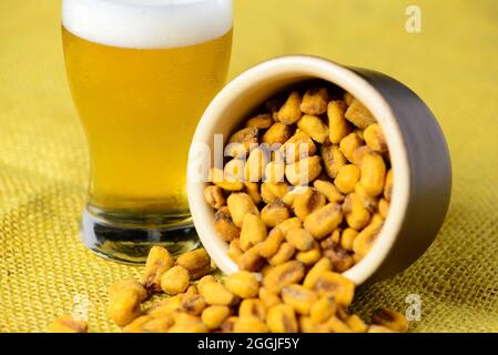Gerösteter und gesalzener Mais im Keramiktopf über gelber Jute und mit einem Glas kaltem Bier Stockfoto