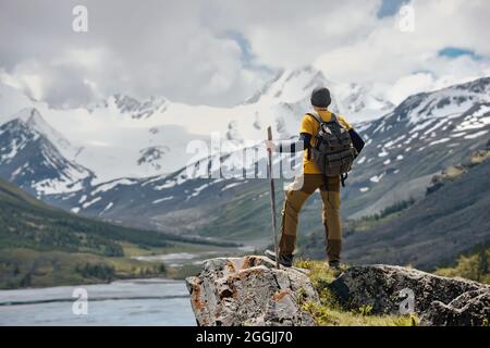 Reisende oder Rucksacktouristen stehen mit Rucksack auf einem großen Felsen und blicken auf Gletscher und Fluss Stockfoto