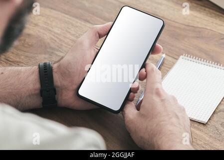 Über die Schulter Blick auf den Mann, der mit einem Smartphone am Holztisch sitzt Stockfoto