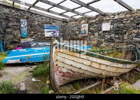 Ein altes, ruiniertes und dachloses Gebäude mit alten Booten bildet eine ungewöhnliche Kunstgalerie in der Skerray Bay an der Nordküste Schottlands direkt vor der NC500. Stockfoto