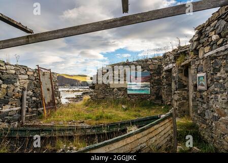 Ein altes, ruiniertes und dachloses Gebäude mit alten Booten bildet eine ungewöhnliche Kunstgalerie in der Skerray Bay an der Nordküste Schottlands direkt vor der NC500. Stockfoto