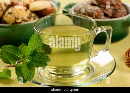 Minztee in transparenter Tasse mit süßen Plätzchen um Stockfoto
