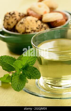 Minztee in transparenter Tasse mit süßen Plätzchen um Stockfoto
