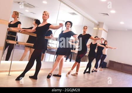 Eine Gruppe von Tänzerinnen führt Ballettübungen durch, indem sie ihre Arme an der Bar im Fitnessstudio hochheben Stockfoto