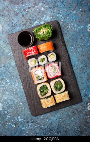 Ansicht der traditionellen japanischen Küche die hellen leckeren Sushi-Brötchen mit Lachs, Kaviar, Avocado, Frischkäse und Sojasauce in schwarzer Schüssel auf blauem Konz Stockfoto