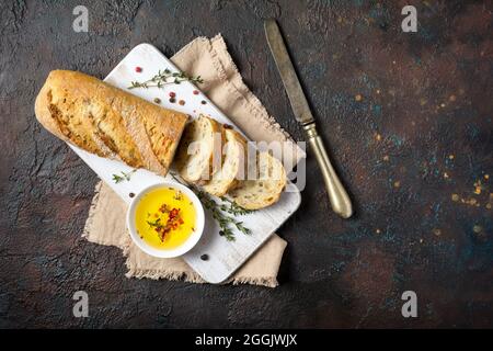 Draufsicht auf frisches Vollkornbrot mit Olivenöl, altem Tafelmesser und Thymiangewürz auf dunklem Grunge-Hintergrund Stockfoto