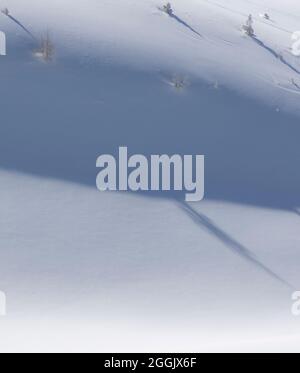 Schatten werfen sich auf den verschneiten Berghang Stockfoto