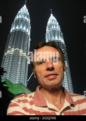 Vertikale Aufnahme eines kaukasischen Mannes, der vor den Petronas-Zwillingstürmen in Malaysia posiert Stockfoto