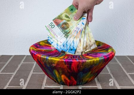 Zürich, Schweiz - 31. Dezember 2020: Eine menschliche Hand lässt einen Haufen schweizer Banknoten in einen Korb mit farbenfrohem Stoff fallen Stockfoto