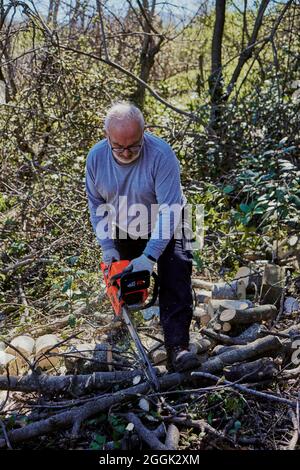 Ein älterer Mann schneidet mit einer Kettensäge Brennholz Stockfoto