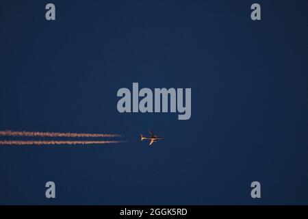 Wunderschöne Teleaufnahme des Flugzeuges am Abend in orangen Farben der untergegangenen Sonne auf dunkelblauem Hintergrund über den Dublin Mountains, Irland Stockfoto