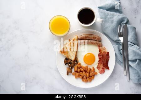 Traditionelles irisches Frühstück. Spiegeleier, gegrillte Würstchen, Pilze, Speck, Bohnen, Kaffee, Saft Stockfoto