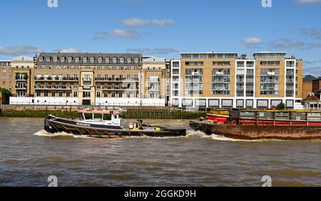 London, England - 2021. August: Industrieschlepper, die einen großen Lastkahn mit Containern auf der Themse schleppen. Stockfoto