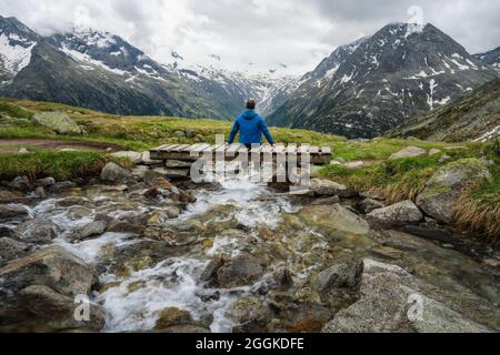 Mann Wanderer auf kleiner Brücke über Berg Fluss am Schlegeis See, Zillertaler Alpen, Österreich ruhen Stockfoto