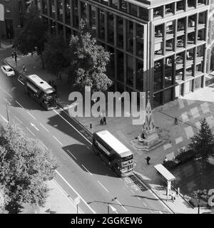 London, Greater London, England, August 24 2021: Schwarz-weiß-Luftaufnahme von zwei Bussen auf einer Straße, während Fußgänger auf dem Bürgersteig laufen. Stockfoto