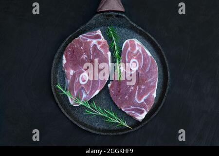 Pfanne mit zwei rohen Lamm Steaks mit Rosmarin bereit zum Kochen. Draufsicht, dunkler Holzhintergrund. Stockfoto