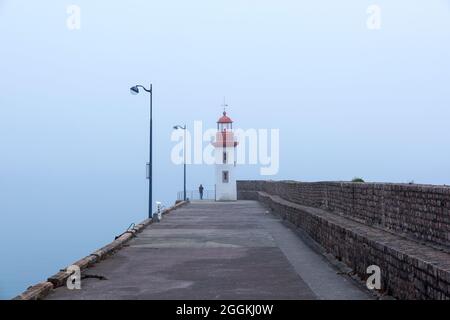 Neblige Stimmung im Hafen von Erquy, Angler am Pier am Leuchtturm, Frankreich, Bretagne, Département Côtes d´Armor, Côte de Penthièvre Stockfoto