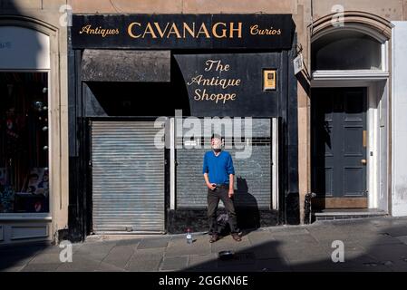 Ein Straßenmusiker, der irische und schottische Balladen vor einem gesperrten Antiquitätengeschäft in der Cockburn Street in der Altstadt von Edinburgh singt. Stockfoto