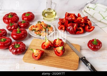 Rote Ratunda-Paprika auf einem hölzernen Schneidebrett über dem Küchentisch vierteln. Rohe gogoshar-Paprika für die Röstung im Ofen vorbereiten. Stockfoto