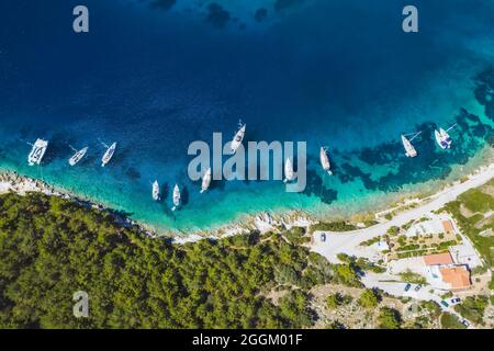 Von oben nach unten Luftaufnahme von Segelbooten, die in der blauen Bucht von Fiskardo, der Insel Kefalonia, Ionisch, Griechenland, angedockt sind, Stockfoto