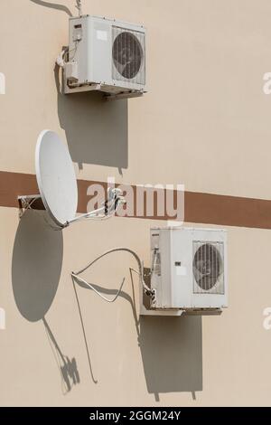 Klimaanlagen und Satellitenschüssel an der Wand eines modernen Hauses auf der Straße im Freien. Stockfoto