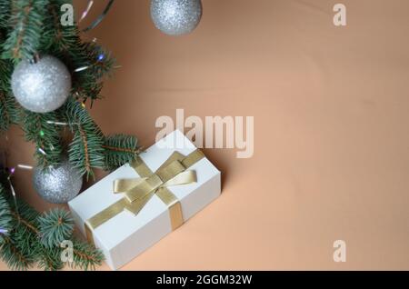 Neujahrsdekoration. Fichtenzweige mit silbernen Kugeln, eine Geschenkbox auf einem beige welligen Hintergrund aus Chiffon. Selektiver Fokus. Stockfoto
