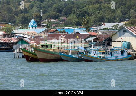 Sorong, Indonesien - 3. Okt 2019: Bescheidene Häuser in Sorong Stadt und alte Fischer- und Frachtboote, die im Hafengebiet, West Papua, festgemacht sind Stockfoto