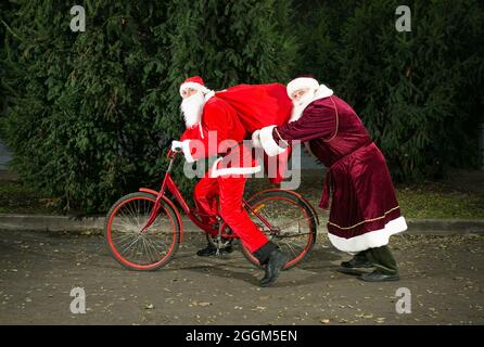 Treffen von zwei Weihnachtsmännern. Einer von ihnen fährt mit dem Fahrrad. Weihnachtsmänner sind in Eile, um Geschenke zu liefern. Stockfoto