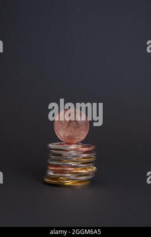 Goldene Bitcoin-Münze mit Bitcoin-Symbol auf einem Stapel verschiedener Bitcoin-Münzen auf dunklem Hintergrund. Stockfoto