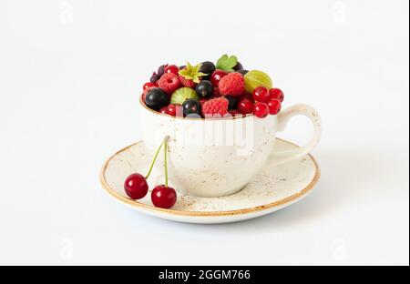 Beeren in einem Becher auf weißem Hintergrund. Kirschen, Himbeeren, Stachelbeeren und rote Johannisbeeren in einer Tasse. Saftig frische Beeren. Gesundes Lebensmittelkonzept. Stockfoto