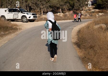 Seit 2004 gehen die Kinder aus dem Dorf Tuba zur Schule im nahegelegenen Dorf at-Tuwani, 2.6 km entfernt - während sie von einem jüdischen Aktivisten und einem Fahrzeug der israelischen Streitkräfte begleitet werden, um sie vor gewalttätigen Angriffen der religiösen jüdischen Siedler aus dem illegalen Außenposten der Maon Farm zu schützen, die auf dem Weg zur Schule gefunden wird. Palästina / Israel, südlich von Hebron. August 2021. (Foto von Matan Golan/Alamy Live News) Stockfoto