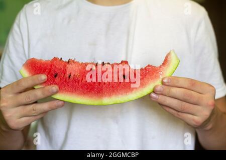 Ein junger Mann isst eine Wassermelone, eine reife Scheibe Wassermelone in den Händen Stockfoto