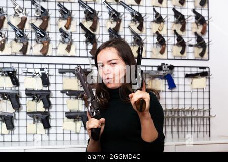 Fröhliche junge Frau, die mit zwei Handfeuerwaffen das Ziel imitiert Stockfoto