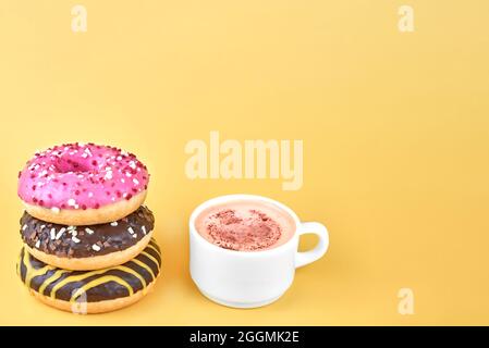 Drei helle Donuts in der Nähe einer Tasse Kaffee. Stockfoto
