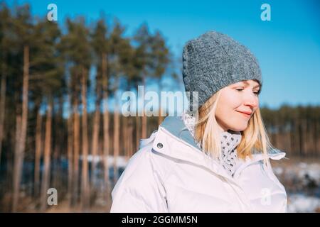 Junge schöne hübsche kaukasische Mädchen Frau gekleidet in weiße Jacke und grau-blau, grauer Hut lächelnd und genießen das Leben im verschneiten Wald im Wintertag Stockfoto