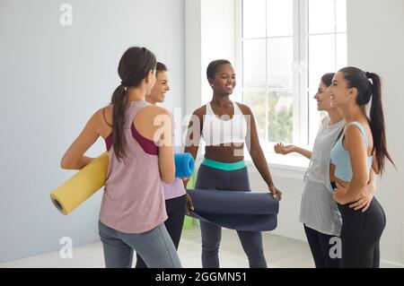 Sportfrauen haben Spaß, miteinander in einem Sportstudio zu kommunizieren, das Fitnessmatten hält. Stockfoto