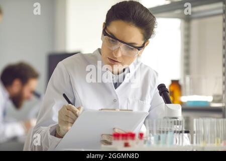 Wissenschaftler, die sich Notizen machen, während sie medizinische Forschung im modernen wissenschaftlichen Labor betreiben Stockfoto