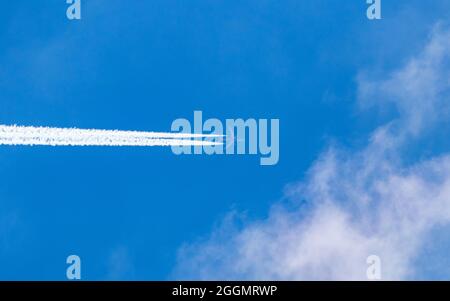 Passagierflugzeuge fliegen in großer Höhe mit Kondensstreifen an leicht bewölkten, sonnigen Tagen. Stockfoto