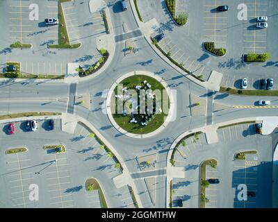 Direkte Luftaufnahme eines 4-Wege-Kreisels im Stadtzentrum, alle Seiten von leicht gefüllten Parkplätzen umgeben. Stockfoto