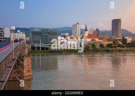 Linz, Österreich. Stadtbild des Flussufers Linz, Österreich bei Sonnenaufgang im Sommer mit Spiegelung der Lichter der Stadt in der Donau. Stockfoto