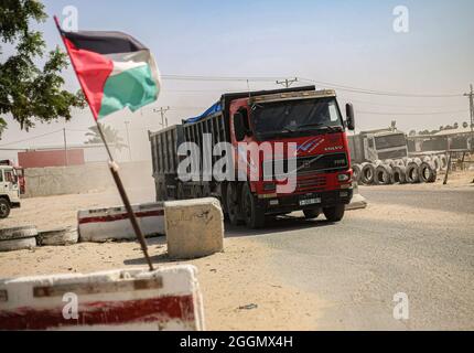 Gaza, Palästina. September 2021. Eine palästinensische Flagge, die mit einem Lastwagen mit Waren im Hintergrund am Güterübergang Kerem Shalom winkt, als Israel eine Reihe von Maßnahmen zur Lockerung der Blockade des Gazastreifens genehmigte, einschließlich der Ausweitung der Fischereizone auf 15 Meilen, Öffnung des Grenzübergangs Kerem Shalom, um die Handelsbewegung zwischen Israel und dem Gazastreifen fortzusetzen, Erhöhung der Wasserquote für den Gazastreifen um 5 Millionen Kubikmeter und Erhöhung der Quote der Händler im Gazastreifen, den Grenzübergang Erez im nördlichen Gazastreifen zu überqueren. Kredit: SOPA Images Limited/Alamy Live Nachrichten Stockfoto