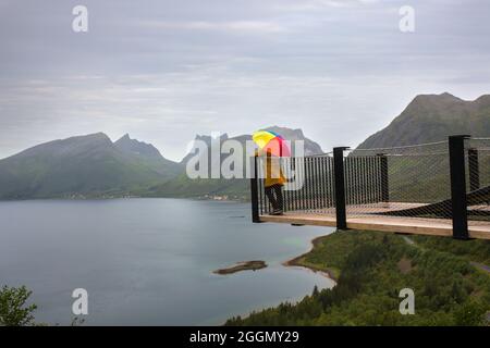 Frau, die am Rande einer 44 Meter langen Aussichtsplattform steht und das Wasser des Bergsfjords überblickt, und die Aussicht auf die Insel Senja im Norden Norwegens genießt Stockfoto