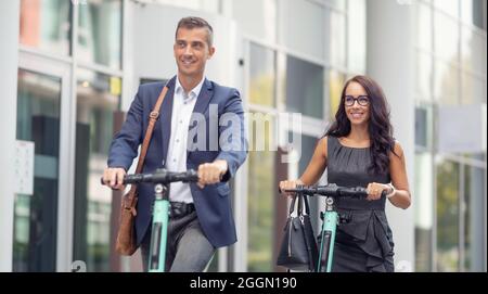 Büromitarbeiter pendeln mit E-Mobility-Elektrorollern auf moderne Weise zur Arbeit. Stockfoto